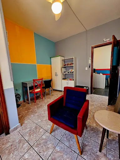 Consultório infantil colorido para sublocação no Espaço Presente com poltrona vermelha, mesa celeste e estante de brinquedos, lousa de giz e materiais lúdicos.